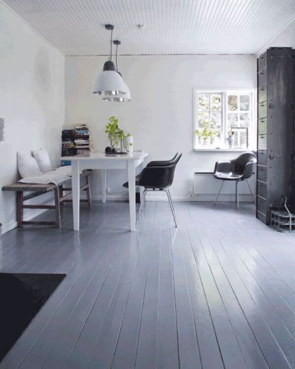 Dining area with gray painted wood floor, white walls, black chairs, and a window letting in natural light.