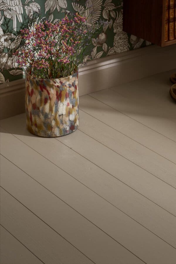 Neutral greige wood floor near floral wallpaper, featuring a colorful vase filled with small pink flowers.
