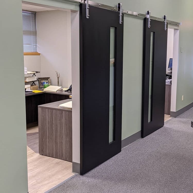 Black sliding barn doors with narrow glass panels in a modern industrial office setting.