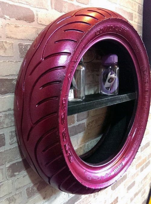 A repurposed pink tire hung on a brick wall, used as a shelf holding two containers