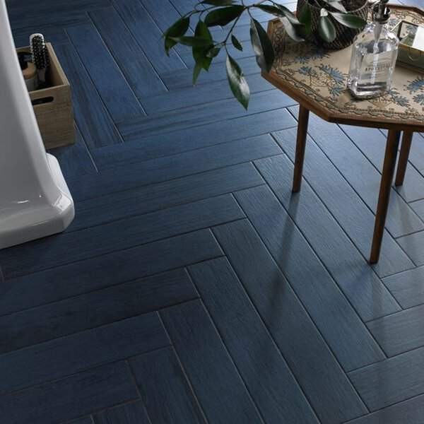 Wood floor in a navy herringbone pattern, shown with a small wooden table and leafy greenery.