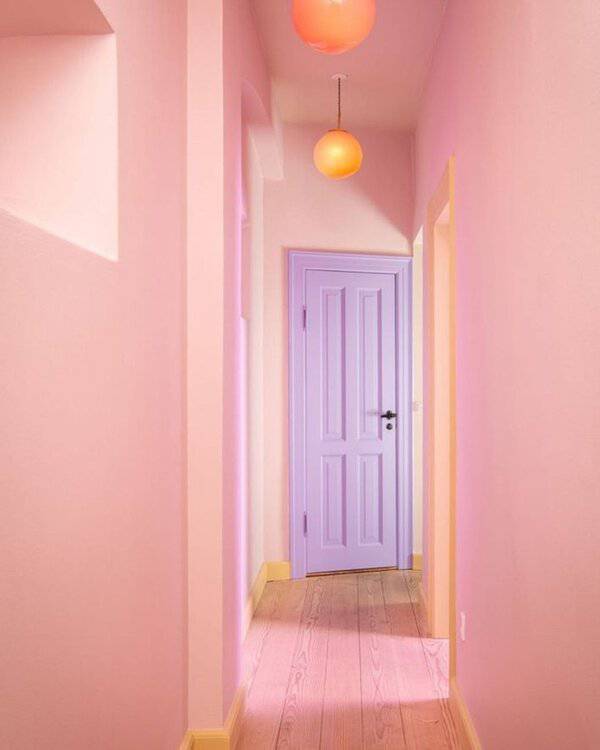 Hallway with pink walls, a lavender door, and bright orange pendant lights over natural wood flooring.