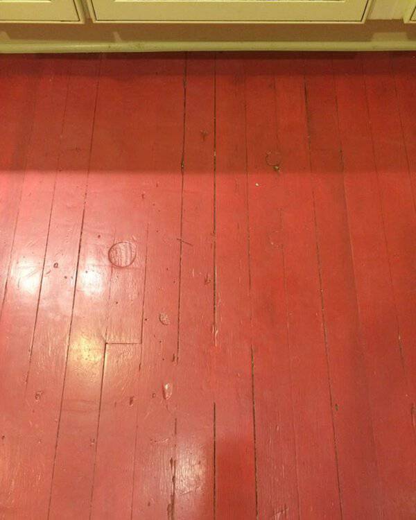 Close-up of bright terracotta painted wood floor with visible wear under light-colored cabinetry.