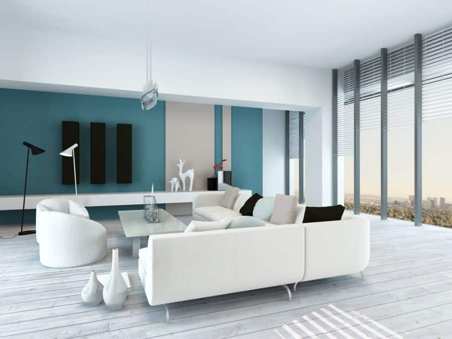 Modern living room with white sofas, a turquoise accent wall, large windows, and minimal decor