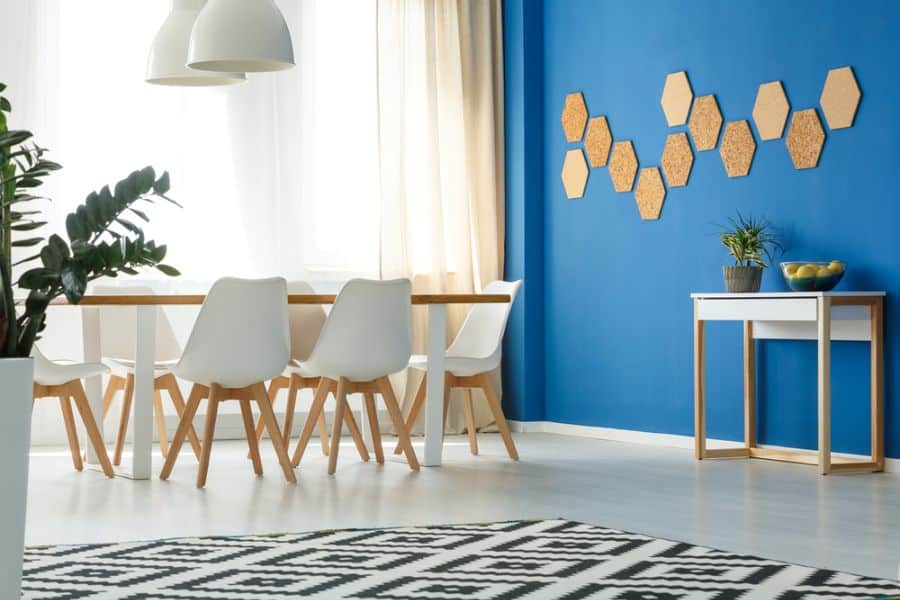 Modern dining room with white chairs, wooden table, accent blue wall, hexagonal decor, and a small table with plants