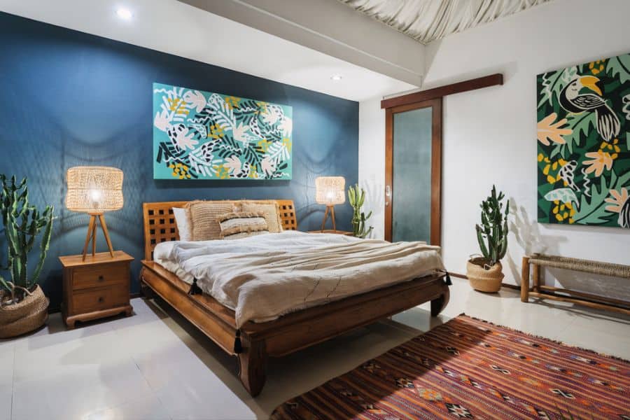 Cozy bedroom with a wooden bed, vibrant wall art, potted plants, and an accent rug on a tiled floor