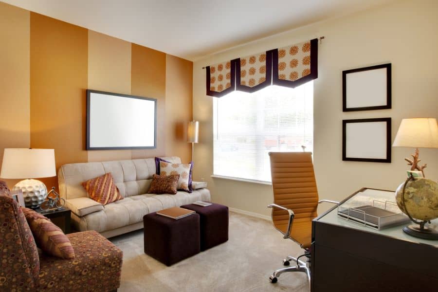 Cozy office with a beige couch, brown chair, and accent wall window featuring geometric drapes