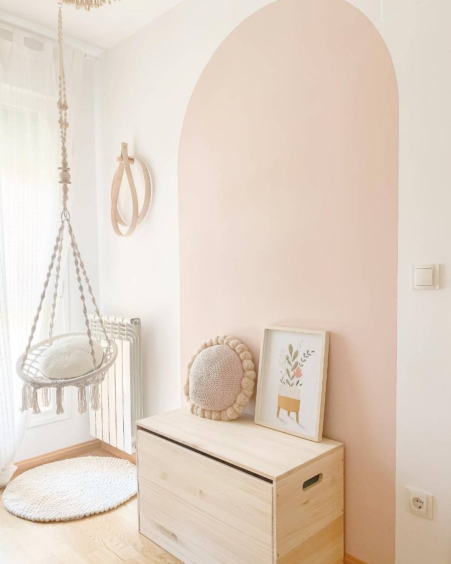 Minimalist room with a hanging chair, wooden chest, and framed artwork on a vibrant pink accent wall