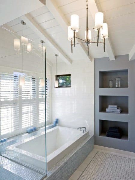 Modern bathroom with shiplap ceiling, built-in bathtub, chandelier, and recessed shelving.