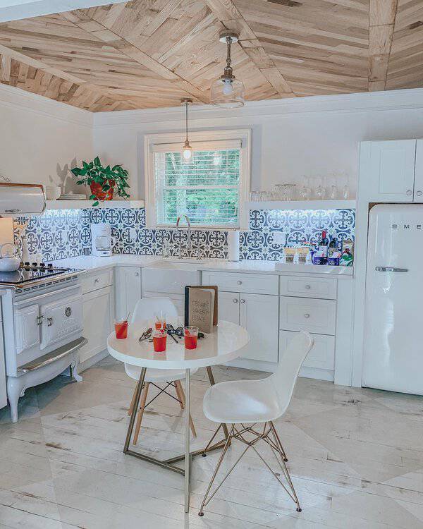 Kitchen with a distressed white painted floor, herringbone wood ceiling, bold tile backsplash, and vintage-inspired appliances.