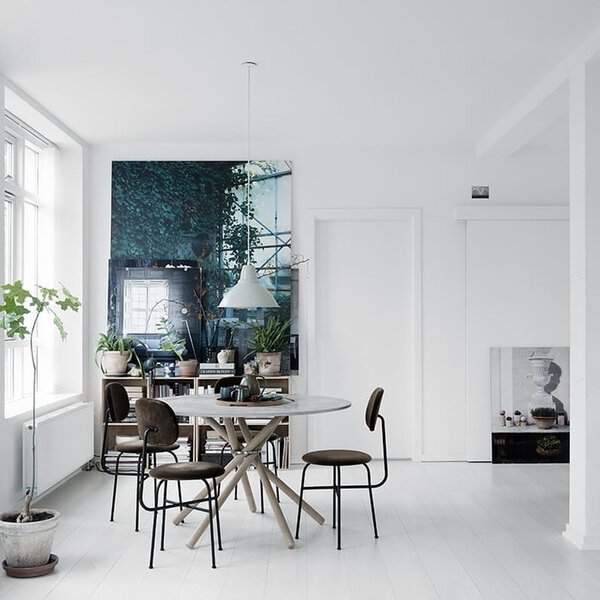 Dining area with white painted wood floor, round table, black chairs, and a large art piece against the wall.