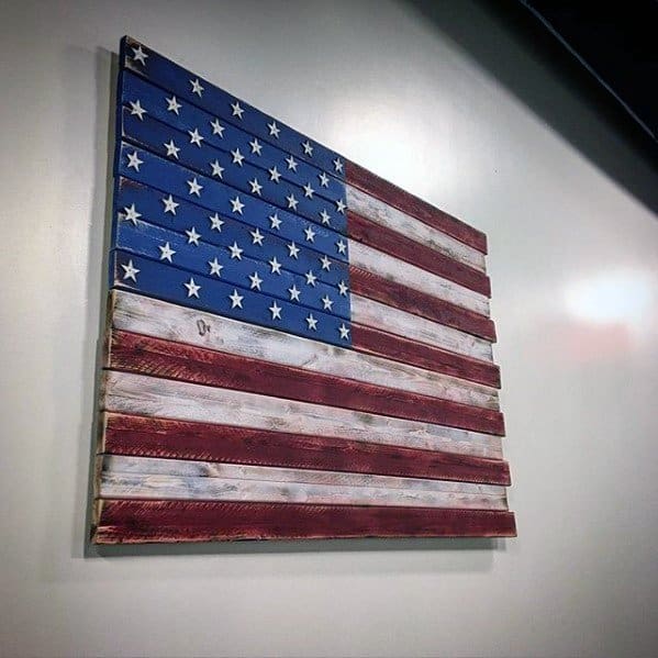 A wooden American flag with weathered red, white, and blue paint hangs on a wall