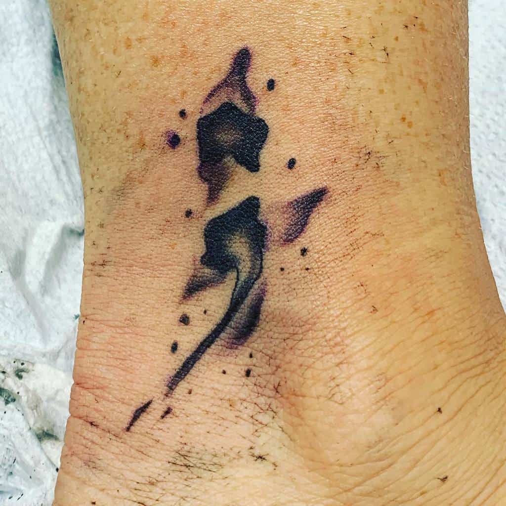 The tattoo features a semicolon design with abstract ink splashes and a flowing, artistic effect around the ankle.