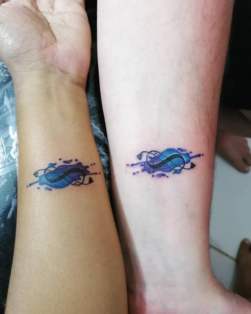 A vibrant infinity tattoo in blue and purple with watercolor splashes, symbolizing endless connection and creativity.