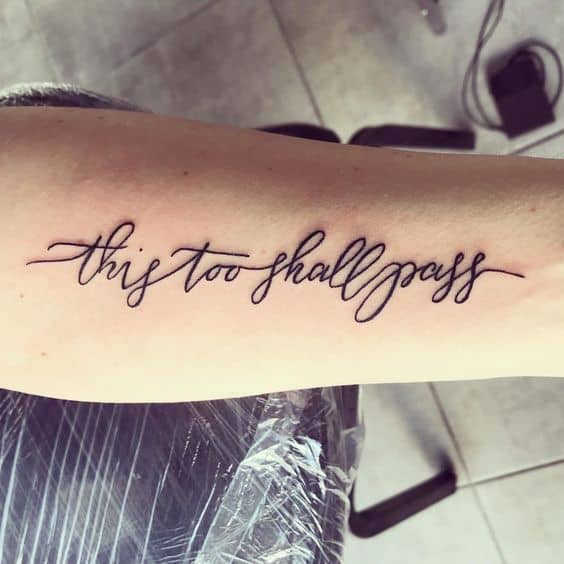 "This too shall pass" tattoo in cursive on the forearm.