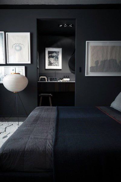 Minimalist grey bedroom with dark walls, abstract art, and a tripod floor lamp, cozy bed with dark bedding in foreground