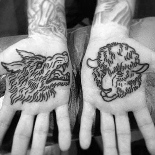 Black wolf and sheep tattoos on the palms of two hands, positioned side by side