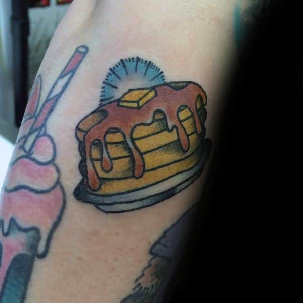Traditional-style pancake tattoo with syrup, butter, and a subtle sunburst effect, featuring bold outlines and vibrant shading for a classic look.