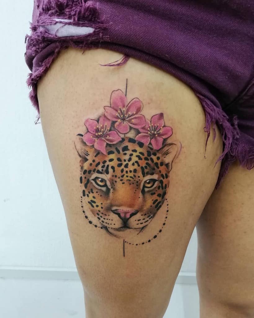 A colorful tattoo of a jaguar's face adorned with pink flowers on top, placed on the thigh with soft shading and vibrant details.