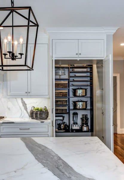 White pantry cabinet with pull-out drawers, appliances, and wicker baskets.