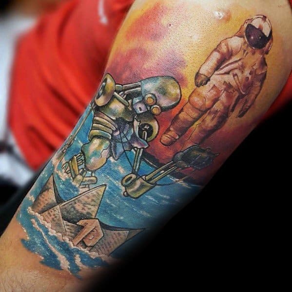 Vibrant tattoo featuring a paper boat, astronaut, and robot over water, symbolizing exploration, adventure, and the fusion of imagination.