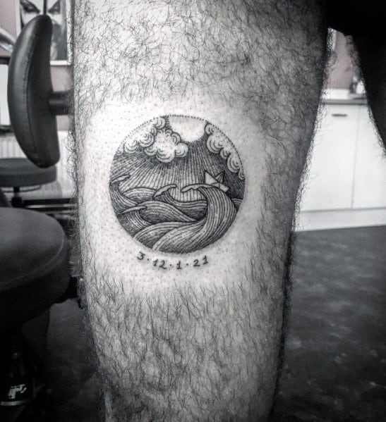Black ink circular tattoo of a paper boat on waves under a cloudy sky, with a date below, symbolizing life's journey and resilience.
