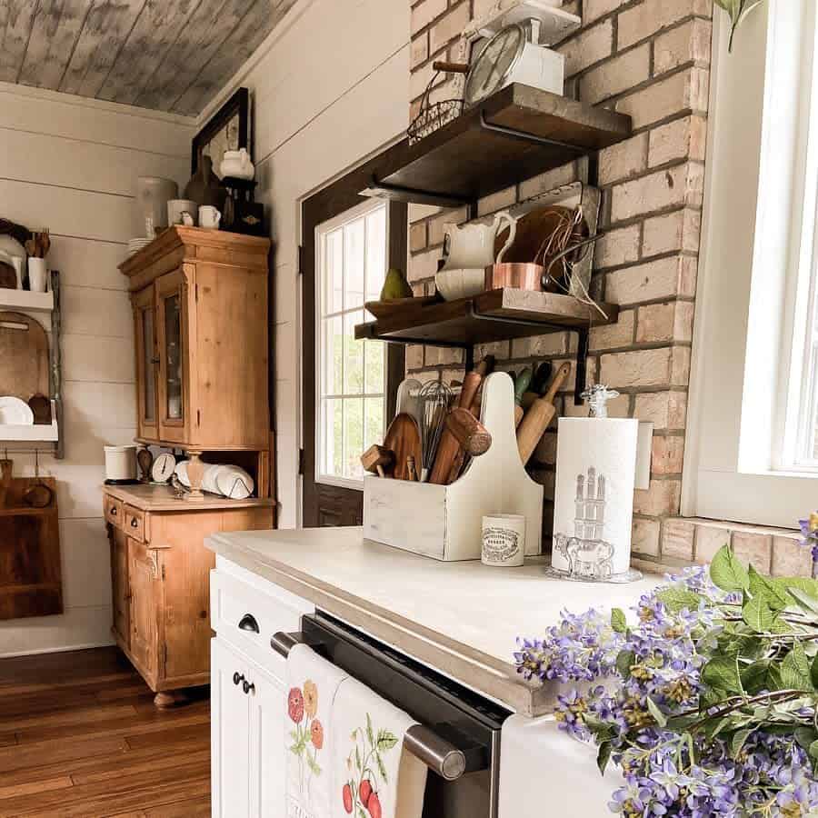 glass paper towel holder in rustic kitchen with wood cabinets and brick wall