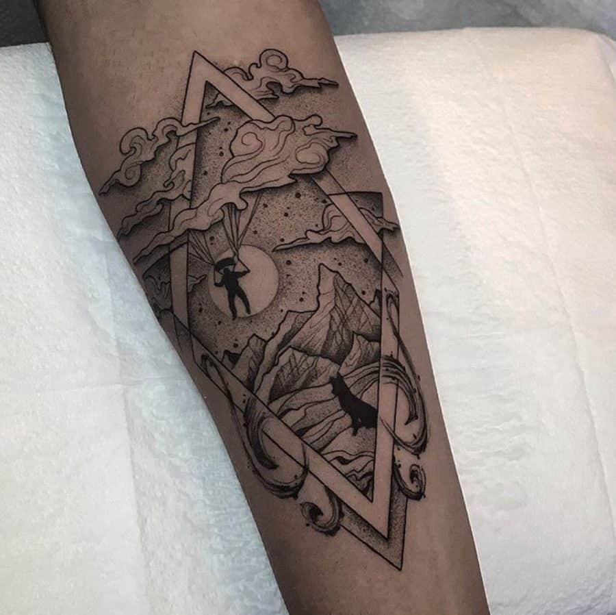 Forearm tattoo featuring a geometric frame with mountains, a wolf howling, a parachutist, and swirling clouds, blending nature and surreal elements.