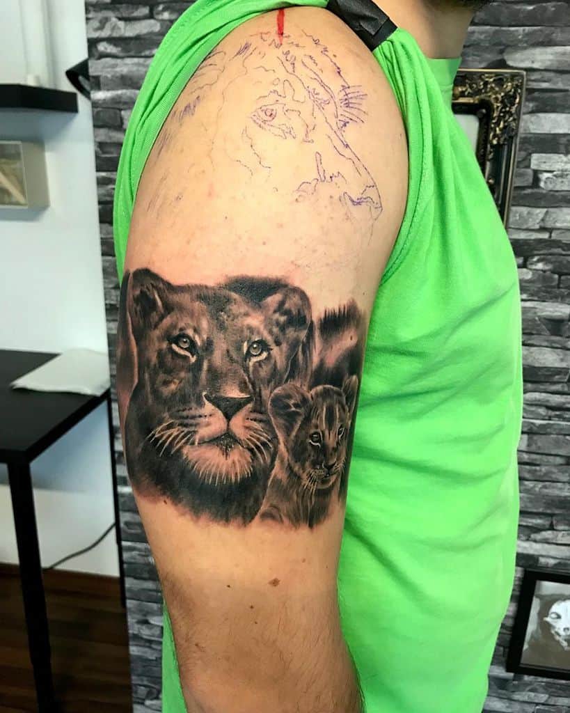 Black and grey upper arm tattoo featuring a realistic lioness and cub, symbolizing strength, protection, and maternal love.