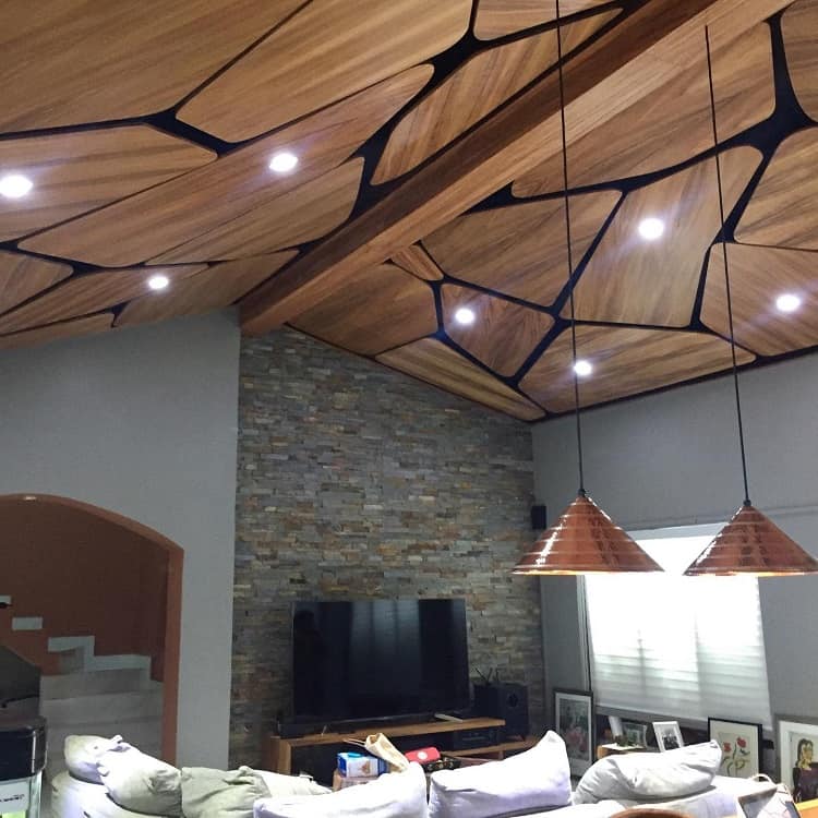 A stylish living room with a parota wood suspended ceiling, unique geometric patterns, integrated lighting, and a stone accent wall, creating a modern and cozy atmosphere