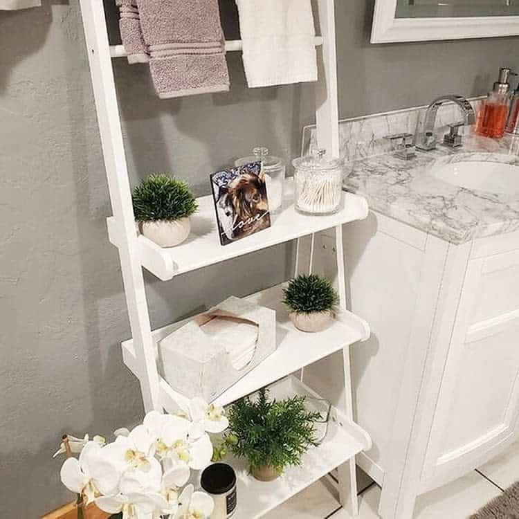White tiered bathroom shelving unit with towels, plants, and decorative items.