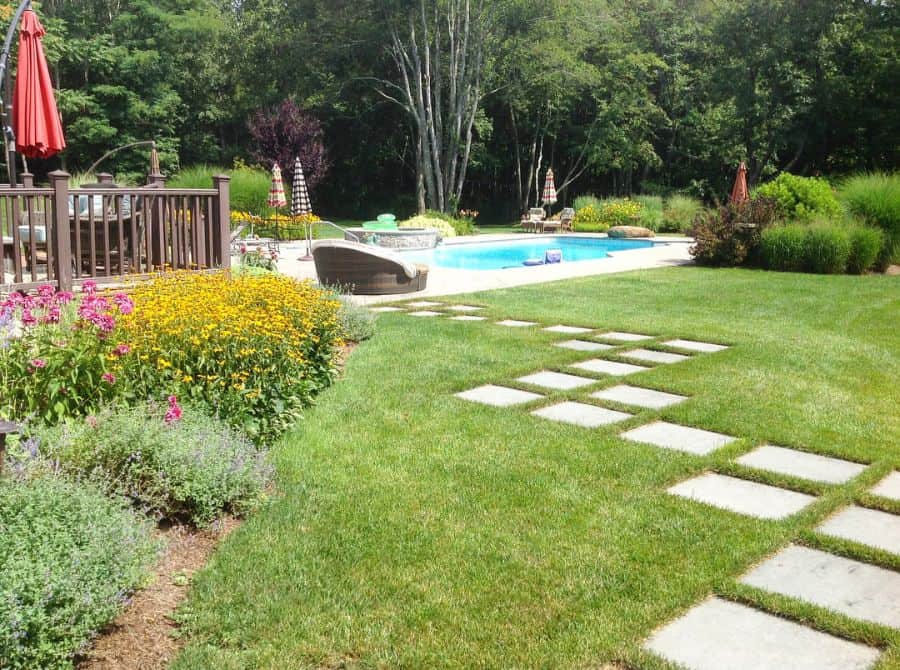 large backyard paver path through grass to pool patio wood deck