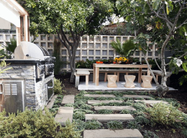 Backyard with a wooden dining set, stone path, built-in BBQ grill, and lush greenery