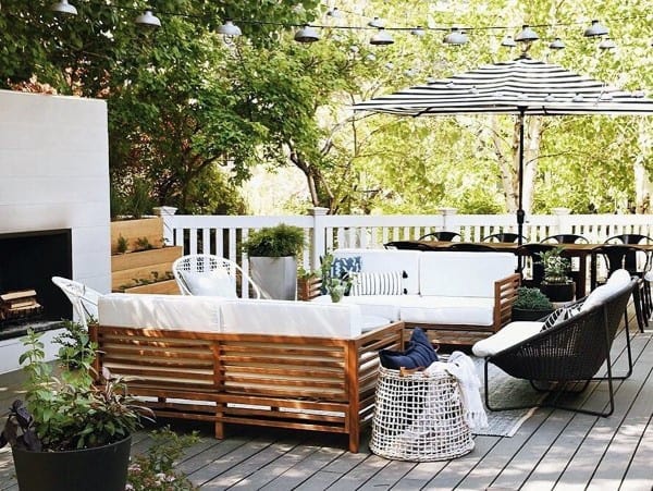 Charming patio with wooden furniture, white cushions, a striped umbrella, string lights, and lush greenery