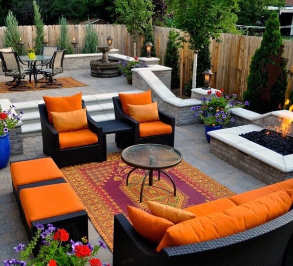 Cozy patio with orange furniture, a fire pit, and colorful plants against a wooden fence