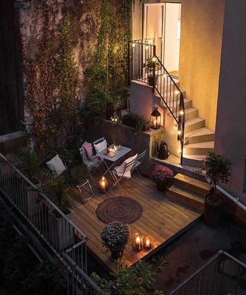Cozy patio with chairs, table, candlelight, and plants at night, nestled beside stairs with warm lighting