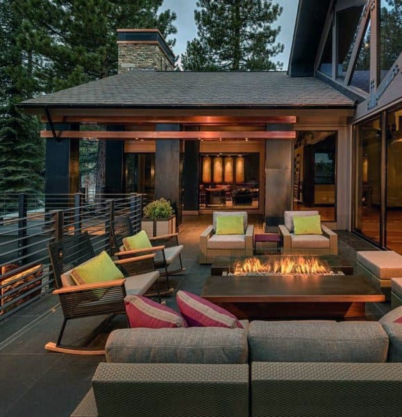 Modern patio features a cozy fire pit, cushioned seating, and trees in the background