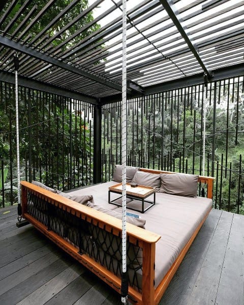 Contemporary outdoor hanging bed with wooden frame, cushions, and a sleek pergola design.