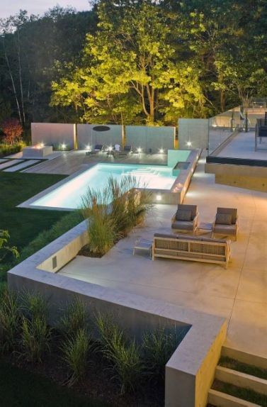 Modern outdoor patio pool area with lounge chairs, surrounded by greenery and ambient lighting at dusk