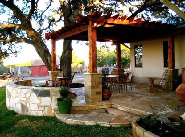 Outdoor patio with wooden pergola, stone seating area, patio dining set, and lush greenery and trees