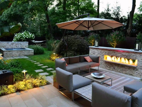 Cozy patio with gray seating, a fire feature, umbrella, and lush garden plus pool and hammock in the background