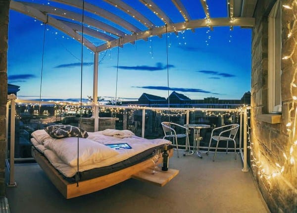 Rooftop hanging bed with fairy lights, cozy bedding, and a stunning evening cityscape view.