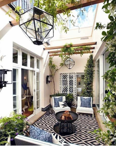 Cozy patio featuring white furniture, a patterned rug, lanterns, and greenery under a charming wooden pergola