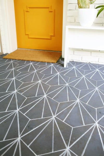 Geometric-patterned tiles flow into a concrete floor, leading to an orange door with a doormat and white plant stand