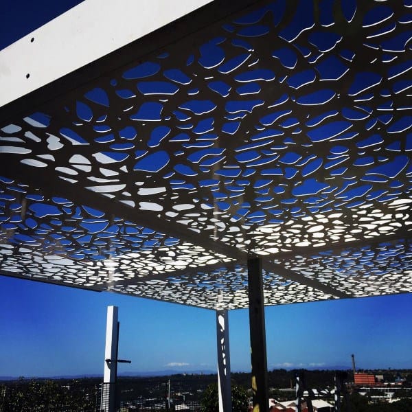 Modern pergola with abstract-patterned steel roof against a clear blue sky.