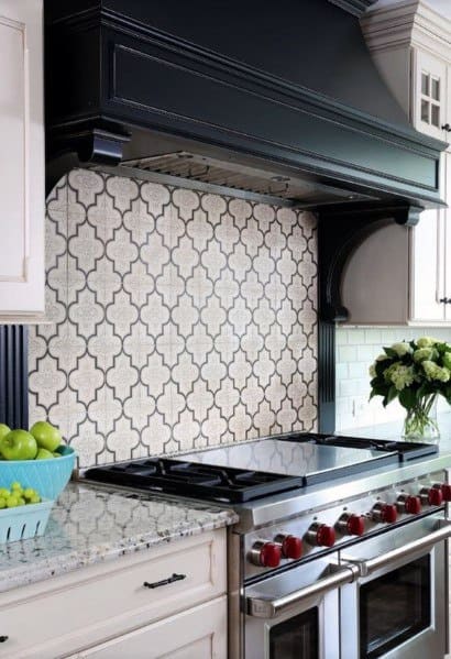 Chic kitchen with a patterned tile backsplash, black range hood, stainless steel appliances, and granite countertops