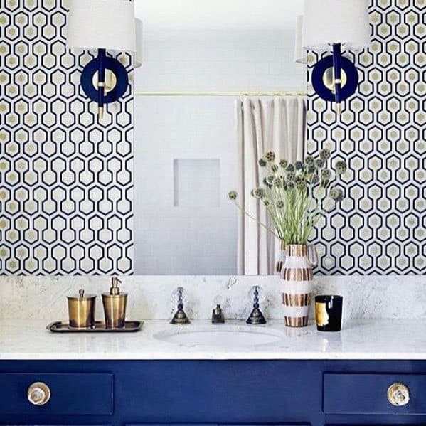 Bathroom with navy vanity, geometric patterned walls, white countertop, and gold accents.