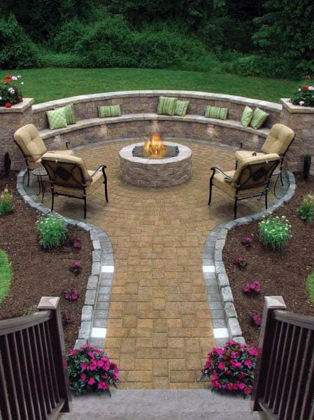 Circular patio with a fire pit, surrounded by cushioned seating and greenery. Stone path leads from the stairs