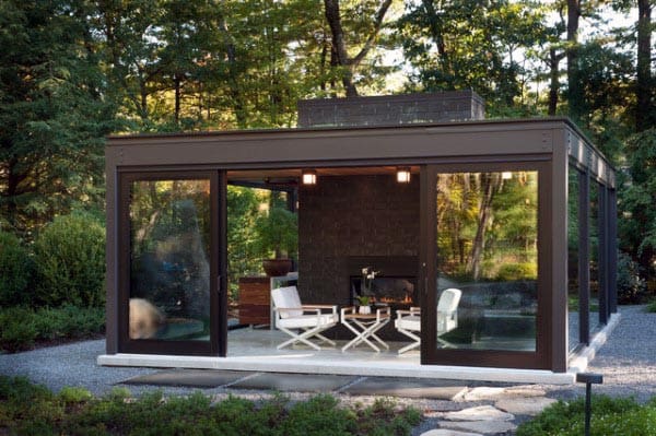Glass-enclosed pavilion with a modern fireplace and minimalist seating, surrounded by a tranquil garden.
