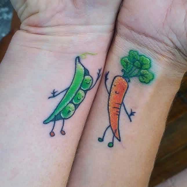 Matching tattoos of a smiling pea pod and carrot with tiny arms and legs, placed on wrists, creating a cute and playful vegetable duo design.